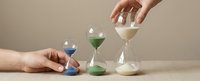 Hands manipulating colorful sand hourglasses showing time management and deadline concepts for business productivity and scheduling applications.