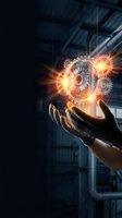 Hand holding glowing gears and cogs with orange light effects against industrial background. Represents innovation, technology, engineering, and business solutions for corporate presentations.