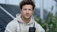 Confident Caucasian man in beige hoodie standing near solar panels with walkie-talkie, representing renewable energy industry professional.