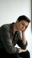 Stressed young Caucasian man holding head in hand showing depression, anxiety and mental health struggles in casual shirt against neutral background.