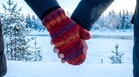 Couple holding hands in colorful knitted mittens against snowy winter forest backdrop, romantic cold weather togetherness and love concept.