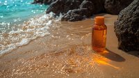 Orange glass bottle on sandy beach with ocean waves and volcanic rocks, sunlight creating warm glow through bottle, foam washing ashore in tropical setting.