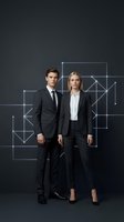 Professional business team of young Caucasian man and woman in formal suits standing against dark background with geometric network pattern.