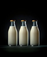 Three glass milk bottles with golden caps arranged on dark surface against black background for dairy product marketing and food photography.