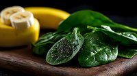 Fresh spinach leaves with water drops and sliced banana on dark wooden board, moody food photography with natural lighting and selective focus.