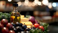 Fresh ingredients with olive oil bottle, vegetables and herbs on kitchen counter with warm bokeh lights creating cozy cooking atmosphere for culinary preparations.