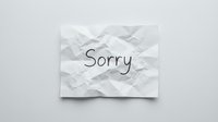 Crumpled white paper note with the handwritten word Sorry on a light gray background, conveying apology, regret, and emotion.