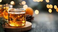 Glass of whiskey on wooden coaster with pine branches, pinecone and warm bokeh lights creating cozy winter holiday atmosphere. Festive drink setting.