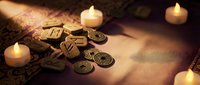 Ancient fortune telling scene with tarot cards, runes and burning candles creating mystical atmosphere for divination and spiritual guidance sessions.