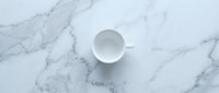 Empty white cup on marble surface, top view for beverage, coffee, or kitchen design projects.