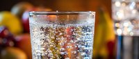 Sparkling water with bubbles in clear glass on blurred restaurant background with warm bokeh lights creating refreshing drink atmosphere.