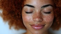 Young African American woman with natural curly red afro hair and freckles smiling with closed eyes, showing natural beauty and confidence in close-up portrait.