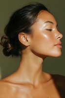 Young Asian woman with glowing skin and natural makeup in profile view, eyes closed peacefully against olive background, hair in elegant bun showing graceful neck line.