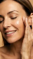 Young woman applying facial moisturizer cream with gentle massage movements, smiling with eyes closed during daily skincare routine for healthy glowing skin.