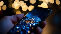 Smartphone displaying night cityscape with bokeh lights reflection, hand holding mobile device against blurred golden background. Modern technology concept.