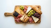 Gourmet charcuterie board with assorted cheeses, cured meats, grapes, olives and crackers on wooden cutting board for entertaining and appetizers.