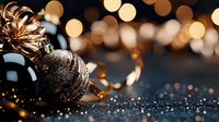 Glittering black Christmas bauble with golden ribbon on dark surface against blurred bokeh lights background creates festive holiday atmosphere.
