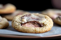 Soft baked sugar cookie with melted chocolate candy center on gray surface, shallow depth of field macro photography shows gooey texture and golden edges.