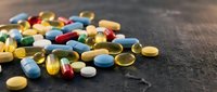 Colorful pharmaceutical pills and capsules scattered on dark wooden surface for medical healthcare and medication concepts.