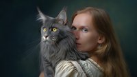 Young woman with long blonde hair in vintage dress holding majestic grey Maine Coon cat with yellow eyes against dark green background in classical portrait style.