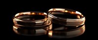 Rose gold wedding bands with elegant grooved design on black reflective surface, romantic symbol of eternal love and commitment captured in soft lighting.
