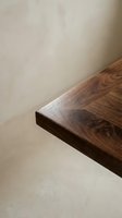 Close-up of polished walnut wood table edge showing rich grain patterns and smooth finish against neutral beige wall background for interior design.