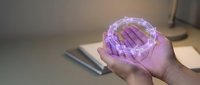Caucasian male hand holding transparent purple geometric crystal sphere with faceted surface on blurred office desk background with notebook and pen.