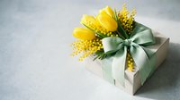 Gift box with yellow tulips and mimosa flowers decorated with green ribbon bow on gray background for spring holidays and celebrations.