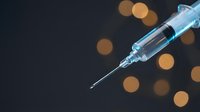 Medical syringe with needle against dark background with warm bokeh lights for healthcare and vaccination concepts.