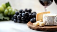 Soft brie cheese with dark grapes and red wine on wooden board, selective focus composition for gourmet food and wine pairing presentation.