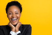 Young African American businesswoman with natural hair laughing joyfully with hands on face against vibrant yellow background, expressing genuine happiness.
