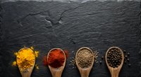 Colorful spices in wooden spoons arranged on dark slate background. Turmeric, paprika, coriander seeds and black peppercorns for cooking and seasoning.
