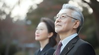 Senior Asian businessman with glasses and woman colleague looking up outdoors, confident expressions, professional attire, natural light.