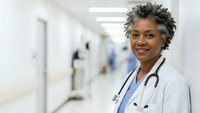 Confident African American female doctor with stethoscope smiling in modern hospital corridor. Professional healthcare worker in white coat for medical concepts.