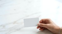 Hand holding blank white business card against marble surface for branding mockup and corporate identity design presentation.