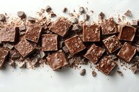 Broken dark chocolate squares with sea salt scattered on white surface, creating dramatic composition with crumbs and pieces. Food photography background.