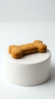 Dog bone-shaped treat resting on white ceramic pedestal against neutral background. Crunchy biscuit snack for pets, ideal for training, rewards, and promotional pet care content.