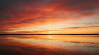 Dramatic sunset over calm water with vibrant orange and red sky reflecting on still lake surface, ideal for nature and landscape backgrounds.