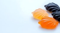 Colorful fruit-flavored jelly candies in shell shapes on white background, featuring orange, yellow, and black varieties for confectionery designs.