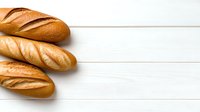 Fresh baked golden French baguettes arranged on white wooden background with copy space, top view. Traditional crusty bread loaves for food design.