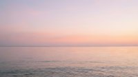 Serene ocean horizon at sunrise with soft pink and purple sky reflecting on calm water surface, suitable for wellness and travel backgrounds.