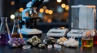 Laboratory setup with microscope, mineral specimens, crystals and chemical glassware for geological research and scientific analysis in modern lab environment.