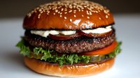 Juicy beef burger with fresh vegetables and sauce layered between toasted sesame seed bun, macro food photography with selective focus on meat patty.