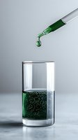 Green liquid drop falling from pipette into glass cylinder with effervescent solution on gray background, minimalist laboratory research concept.