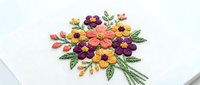 Colorful embroidered flower bouquet with orange, yellow, and purple blooms on white fabric background. Suitable for textile design and craft projects.