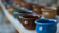 Colorful ceramic pots arranged in row showing handmade pottery collection with brown and blue glazed clay vessels, selective focus on artisanal craftsmanship.