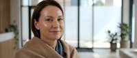 Middle-aged Caucasian businesswoman smiling confidently in modern office environment wearing beige blazer, professional portrait for corporate communications.