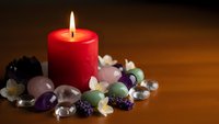 Red candle burning surrounded by colorful healing crystals and gemstones on wooden surface creating peaceful meditation atmosphere for wellness rituals.