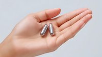Silver metallic capsules on open palm against white background, medical supplement concept for healthcare and wellness marketing, isolated product photography.