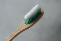 Eco-friendly bamboo toothbrush with white toothpaste and green bristles on neutral gray background, promoting sustainable oral hygiene products.